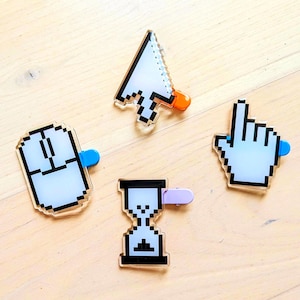 Könnte beinhalten: Vier pixelige Acrylstifte in Form von Computer-Cursorn und -Symbolen. Das Set enthält eine Maus, eine Sanduhr, eine zeigende Hand und einen Pfeil-Cursor. Jeder Stift hat eine unterschiedlich farbige Rückseite, darunter Blau, Orange und Lila.
