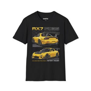 May include: Black t-shirt featuring a yellow RX7 FD3S car graphic. The design includes two illustrations of the car, with the text "RX7 FD3S" and "ROTARY POWER". The shirt has a crew neck and short sleeves.
