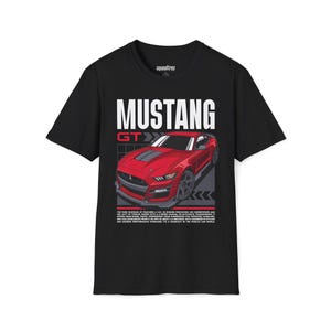 May include: Black t-shirt featuring a red Mustang GT car graphic. The design includes the word "MUSTANG" in large white letters, with "GT" in red. The shirt also has text describing the car's features.