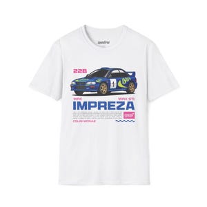 May include: White t-shirt featuring a blue Subaru Impreza rally car graphic. The design includes the number 1, the text "WRC IMPREZA WRX STI", and the name "COLIN MCRAE". The graphic is in blue, gold, and pink.