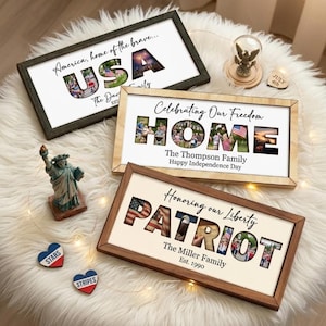 May include: Three framed patriotic artworks with the words "USA", "HOME", and "PATRIOT" in a cutout style, filled with images. The frames are in dark green, light wood, and brown. Additional decorations include a Statue of Liberty figurine and heart-shaped ornaments.