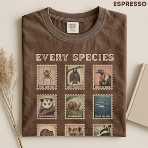 Puede incluir: Una camiseta color marrón espresso con el texto EVERY SPECIES y una cuadrícula de nueve ilustraciones de sellos postales. Cada sello representa un animal con una etiqueta: PEST CONTROL, NIGHT POLLINATOR, CLEAN-UP CREW, SEED DISPENSER, DECOMPOSER y OCEAN BALANCE.