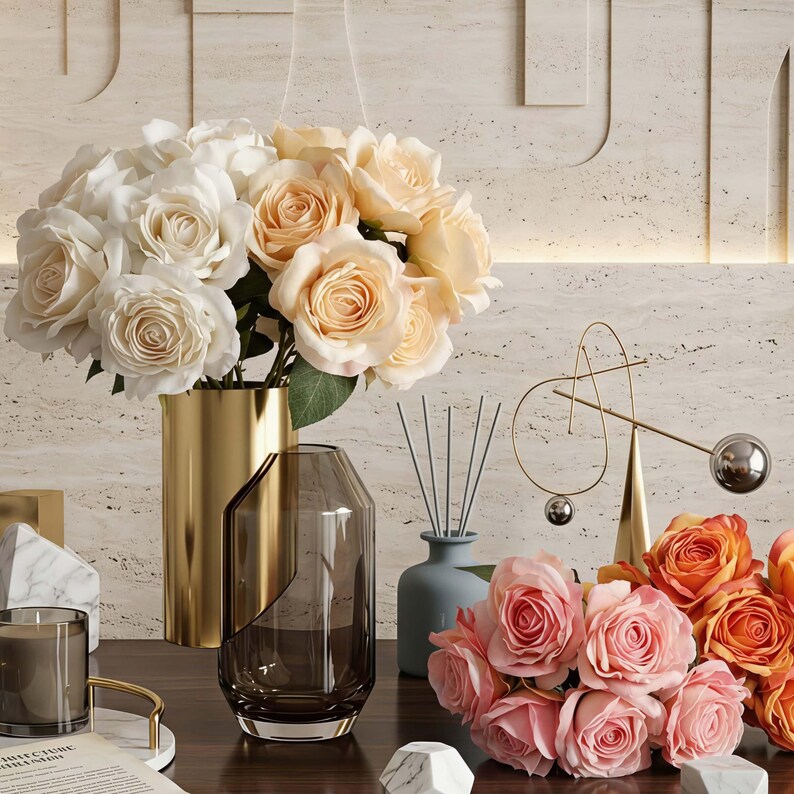 May include: A display of home decor items including bouquets of white, peach, and orange roses in gold and glass vases. A candle, decorative objects, and a diffuser are also present, creating an elegant and stylish arrangement.