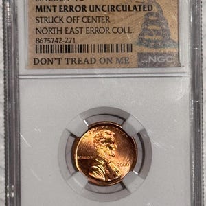 May include: A copper 2000 Lincoln penny, graded and encased in a clear plastic holder. The holder has a label with text: "LINCOLN 1C MINT ERROR UNCIRCULATED STRUCK OFF CENTER DON'T TREAD ON ME".