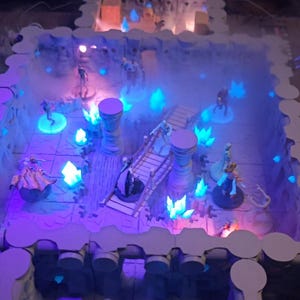 May include: A detailed tabletop gaming scene with miniature figures, a bridge, and glowing blue crystals. The terrain is a multi-level structure with a white and gray color scheme, illuminated by blue and purple lights, creating a fantasy atmosphere.