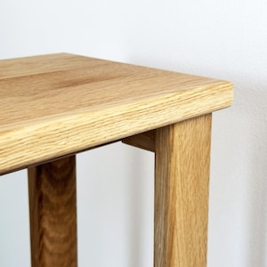 May include: Close-up of a light-colored wooden table. The table has a rectangular top and four sturdy legs. The wood grain is visible, and the table appears to be made of solid wood. The table is likely for indoor use.