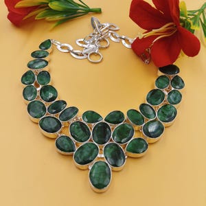 May include: A statement necklace featuring multiple oval-shaped, faceted dark green stones set in polished silver-toned metal settings. The stones are arranged in a tiered, layered pattern, connected by a silver-toned chain with a circular clasp.