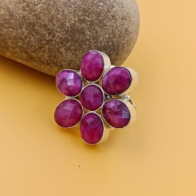 Op de afbeelding: Een zilveren ring met een bloemvormig cluster van zes gefacetteerde, ovaal geslepen magenta robijnen. De centrale steen is omringd door vijf identieke bloemblaadjes, allemaal gezet in een gepolijst zilveren metalen frame met een band.