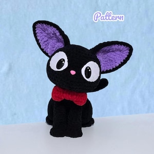 Könnte beinhalten: Eine handgefertigte schwarze Häkelkatze mit großen weißen Augen, einer rosa Nase und einer roten Fliege. Die Katze hat große Ohren mit lila Innenfutter. Das Wort "Pattern" steht in hellvioletter Farbe in der oberen rechten Ecke. Die Katze sitzt auf einer weißen Oberfläche vor einem hellblauen Hintergrund.