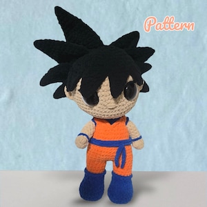 Könnte beinhalten: Gehäkelte Puppe einer Figur mit stacheligen schwarzen Haaren, großen Augen und einem orangefarbenen und blauen Outfit. Die Puppe hat ein hellbraunes Gesicht und trägt einen blauen Gürtel. Das Wort "Pattern" steht in kursiver Schrift oben rechts.