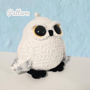 Könnte beinhalten: Ein weißes gehäkeltes Eulenplüschtier mit großen schwarzen Augen und gelben Akzenten. Die Eule hat schwarze Füße und einen kleinen Federbüschel auf dem Kopf. Das Wort "Pattern" ist in kursiver Schrift in der oberen linken Ecke geschrieben.