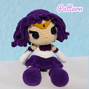 May include: A handmade crochet doll with a purple hairstyle, a gold crown, and large black eyes. The doll wears a white top with purple accents, a purple skirt, and matching purple shoes. The word "Pattern" is written in the top right corner.