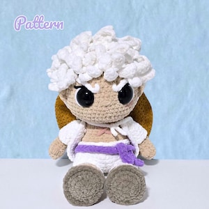 Peut inclure: Poupée au crochet faite à la main avec des accents blancs, beiges et violets. La poupée a de grands yeux noirs, des cheveux bouclés blancs et porte une tenue blanche avec une ceinture violette. Le mot "Pattern" est visible.