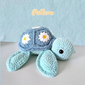 Könnte beinhalten: Gehäkelte Schildkröte in Blau- und Weißtönen. Der Schildkrötenpanzer ist hellblau mit weißen Gänseblümchen-Akzenten. Der Text "Pattern" befindet sich oben. Die Schildkröte hat einen hellblauen Kopf, Flossen und ein schwarzes Auge.