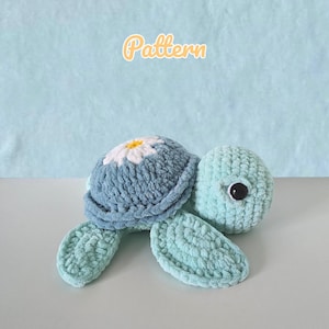 Könnte beinhalten: Eine handgefertigte Plüschschildkröte in Blau- und Grüntönen. Der Schildkrötenpanzer ist ein weiches Blau mit einem weißen und gelben Gänseblümchen-Design. Der Text "Pattern" befindet sich oben in der Mitte des Bildes.
