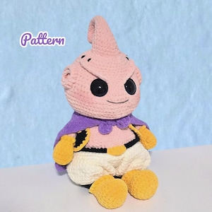 Può includere: Un peluche all'uncinetto fatto a mano di un personaggio con una testa rosa, un mantello viola e guanti e piedi gialli. Il personaggio ha grandi occhi neri e un piccolo sorriso. La parola "Pattern" è scritta in alto a sinistra.