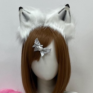 May include: A mannequin head displays a white faux fur headband with black-tipped ears, a brown wig, and a silver bow. A pink fluffy tail with black bands and two pink ornaments are on the left. A star pendant necklace completes the ensemble.