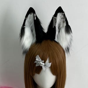 Könnte beinhalten: Ein Cosplay-Set mit schwarz-weißen Fuchsohren mit silbernen Akzenten, einer braunen Perücke und einem rosa Kunstfellschwanz. Das Set enthält einen silbernen Schmetterlings-Haarclip und eine Sternanhänger-Halskette. Ein rosa Kunstfell-Wrap ist ebenfalls enthalten.