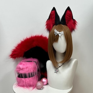 Könnte beinhalten: Ein Cosplay-Set mit roten und schwarzen Fuchsohren, einem passenden Schwanz und rosa, pelzigen Beinwärmern. Die Ohren sind an einer braunen Perücke befestigt. Ein Schaufensterpuppenkopf zeigt das Zubehör, zusammen mit einer silbernen Schleife und einer Sternanhängerkette.