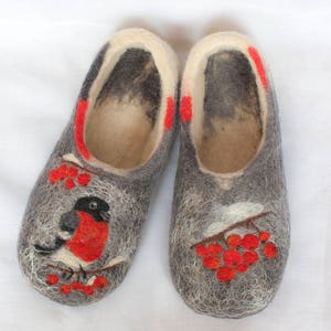 May include: A pair of gray felt slippers with red and white embroidery of a bird and berries. The slippers have a white felt lining.