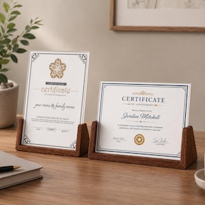 May include: Two clear acrylic certificate holders with dark brown wooden bases. The left holder displays a template with a gold floral emblem and text. The right holder displays a certificate of achievement for Jordan Mitchell with a gold seal.