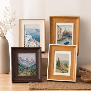 May include: Four rectangular picture frames in varying wood tones, including dark brown, light oak, and white, each containing a different landscape painting featuring scenes of coastal architecture, a Venetian canal, mountains, and a rural countryside.