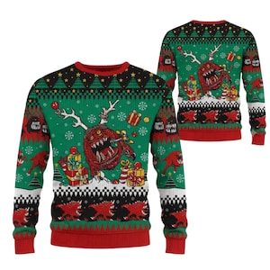 May include: A green long-sleeve jumper featuring a red monster with antlers, surrounded by wrapped gift boxes and snowflakes. The design includes black and white checkered borders, red ribbed cuffs, and a red collar with a repeating tree pattern.