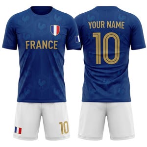 Op de afbeelding: Een blauw voetbalshirt en short set. Het shirt toont "FRANCE" in goud, een Frans vlagembleem en nummer 10. De shorts zijn wit, ook met nummer 10. Een outfit voor voetbalfans.