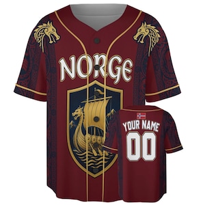 May include: A maroon baseball jersey featuring the text NORGE on the front above a shield graphic with a golden Viking ship. The sleeves have dark patterned panels and gold trim. The back displays the text YOUR NAME, the number 00, and a flag.