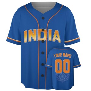 Pode incluir: Uma camisa de beisebol azul com a palavra INDIA em letras degradê laranja e branco na frente. A parte de trás exibe o texto YOUR NAME acima do número 00 em laranja, com um emblema circular gráfico na bainha inferior.