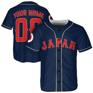 以下が含まれることがあります： 前面に赤文字でJAPAN、背面にYOUR NAMEと背番号00がプリントされたネイビーのベースボールシャツ。フロントはボタン留め仕様で、襟と前立てにはゴールドのパイピングが施されており、袖は半袖のデザインとなっている。