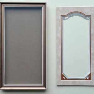 May include: A rectangular frame with a metallic bronze finish and a white inner border surrounding a solid gray center panel, positioned next to a rectangular mirror with a light beige patterned frame and a decorative arched top edge detail.