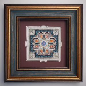 May include: Framed cross-stitch artwork featuring a geometric design with teal, orange, and blue accents. The artwork is set within a double-matted frame with a teal and gold finish, creating a decorative piece.