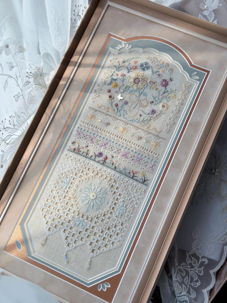 May include: A rectangular framed embroidery sampler featuring intricate needlework with floral motifs, a central butterfly, and geometric lace-like patterns in soft pastel shades of blue, pink, and cream, accented with small beads and crystals.