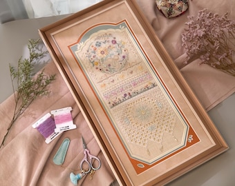 May include: A rectangular framed embroidery sampler featuring intricate floral motifs, geometric patterns, and delicate needlework in soft pastel hues. The artwork is displayed within a light-toned wooden frame with a multi-layered matting border.