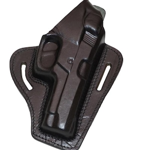 以下が含まれることがあります： 暗い茶色の革製ホルスター。ホルスターには銃が収められており、銃に合うように成形されています。ステッチされたエッジとベルトループが特徴です。銃の一部が見え、銃身とハンドルが見えています。
