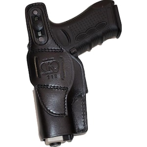 May include: Black leather holster with a firearm inside. The holster has visible stitching and a stamped logo with the number 212. The firearm is black with a textured grip.