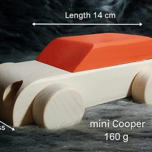 May include: Wooden toy car with an orange roof and natural wood body. The car is 5.5 cm high, 14 cm long, and 8 cm thick. It weighs 160 g. The text "mini Cooper" is visible on the side.