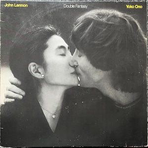 May include: Monochrome album cover showing John Lennon and Yoko Ono in an embrace, kissing. The album is titled "Double Fantasy", with the artists' names above. The image is a close-up, conveying a sense of intimacy and romance.