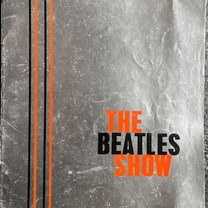 Może przedstawiać: Szara broszura programowa w stylu vintage z napisem THE BEATLES SHOW pomarańczowymi i czarnymi literami. Okładka posiada dwie pionowe czarne linie i dwie pionowe pomarańczowe linie po lewej stronie oraz odręczny tekst na górze K. F. Kirton 2nd Nov 63.