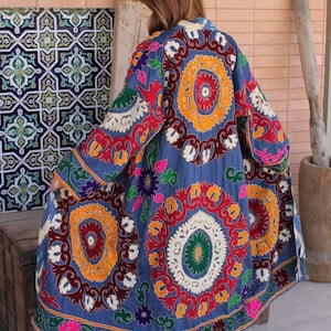 Peut inclure: Long manteau bleu avec broderies colorées complexes. Le manteau présente de grands motifs floraux circulaires dans les tons de rouge, orange, jaune et vert. Les manches et l'ourlet sont également ornés de motifs détaillés.