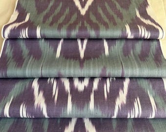 Könnte beinhalten: Gefalteter Stoff mit einem sich wiederholenden Ikat-Muster in Lila-, Grün- und Weißtönen. Der Stoff ist geschichtet und zeigt das komplizierte Design und die Textur. Das Muster hat eine Stammes- oder ethnische Ästhetik.