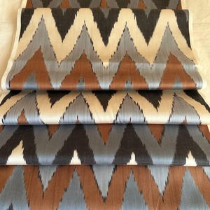 Puede incluir: Varios trozos de tela doblados con un patrón de chevrón repetido. El diseño en zigzag utiliza tonos de negro, gris, marrón y crema. La tela parece ser tejida, posiblemente para proyectos de tapicería o textiles.