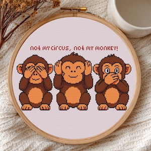 Puede incluir: Bordado de punto de cruz en un aro de madera con tres monos de dibujos animados. Cada mono tiene una pose diferente: cubriendo los ojos, las orejas y la boca. El texto "not my circus, not my monkey!" está arriba.