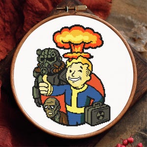 May include: A cross-stitch embroidery in a wooden hoop features a cartoon image of a character with a thumbs-up, a mushroom cloud, and a figure in a gas mask. The color palette includes blue, yellow, red, and black.