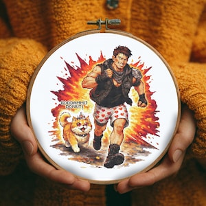 May include: A cross-stitch embroidery hoop featuring a pixelated design of a man running with a dog, set against an orange and red explosion. The man wears a black vest and heart-patterned shorts. The text "GODDAMMIT DONUT!" is above the dog.