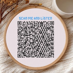 May include: A cross-stitch embroidery hoop with a QR code and the text "SCAN ME AND LISTEN" in blue. The QR code is black and white, and the fabric is white. The wooden hoop is round and has a brass clasp.