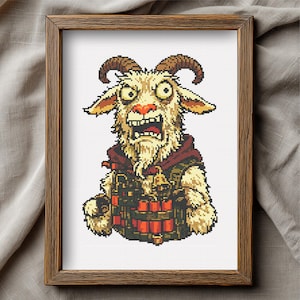 May include: Cross-stitch art of a cartoon goat with a surprised expression, wearing a red hooded vest and holding a bundle of dynamite. The goat has large eyes, brown horns, and a white beard. The artwork is framed in a wooden frame.