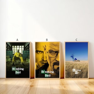 May include: Three framed posters featuring imagery from the television series "Breaking Bad." The posters have a wooden frame. Poster A shows a man in a yellow suit. Poster B features two faces. Poster C shows a camper in a field.