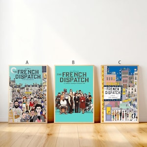 May include: Three framed movie posters for "The French Dispatch" film. Each poster has a different design, with the film's title prominently displayed. The posters are in wooden frames and are displayed against a white wall.